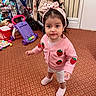 Mia joined the competition — help win amazing prizes! toddler, child, pink_cardigan, headband, strawberry_pattern, carpet, toy_walker, stroller, indoor, floor, toy, person, footwear, curious, young_child, home, cute, standing, expression, clothing