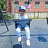 Mia is registered to the contest to win money with this photo: child, toddler, swing, playground, hat, smile, happy, outdoor, sunny, shadow, brick_building, metal_chains, blue_sky, casual_clothing, footwear, fence, pavement, daytime, recreation, fun