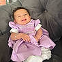 Louanna-Rose is registered to the contest to win money with this photo: baby, infant, smiling, winking, lavender_dress, white_socks, couch, gray_couch, plush_furniture, happy, cute, child, portrait, indoors, hand, face, person, sitting, cozy, casual
