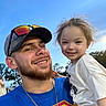 Blaire is registered to the contest to win money with this photo: man, child, smile, outdoor, blue_sky, trees, cap, sunglasses, beard, chain_necklace, casual_clothing, portrait, happy, daylight, holding, family, people, nature, tshirt, sunlight