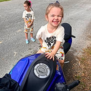 Blaire is registered to the contest to win money with this photo: child, children, motorcycle, road, grass, car, outdoor, smile, happy, person, vehicle, sidewalk, clothing, shorts, tshirt, playful, friendship, toy, helmet, accessory