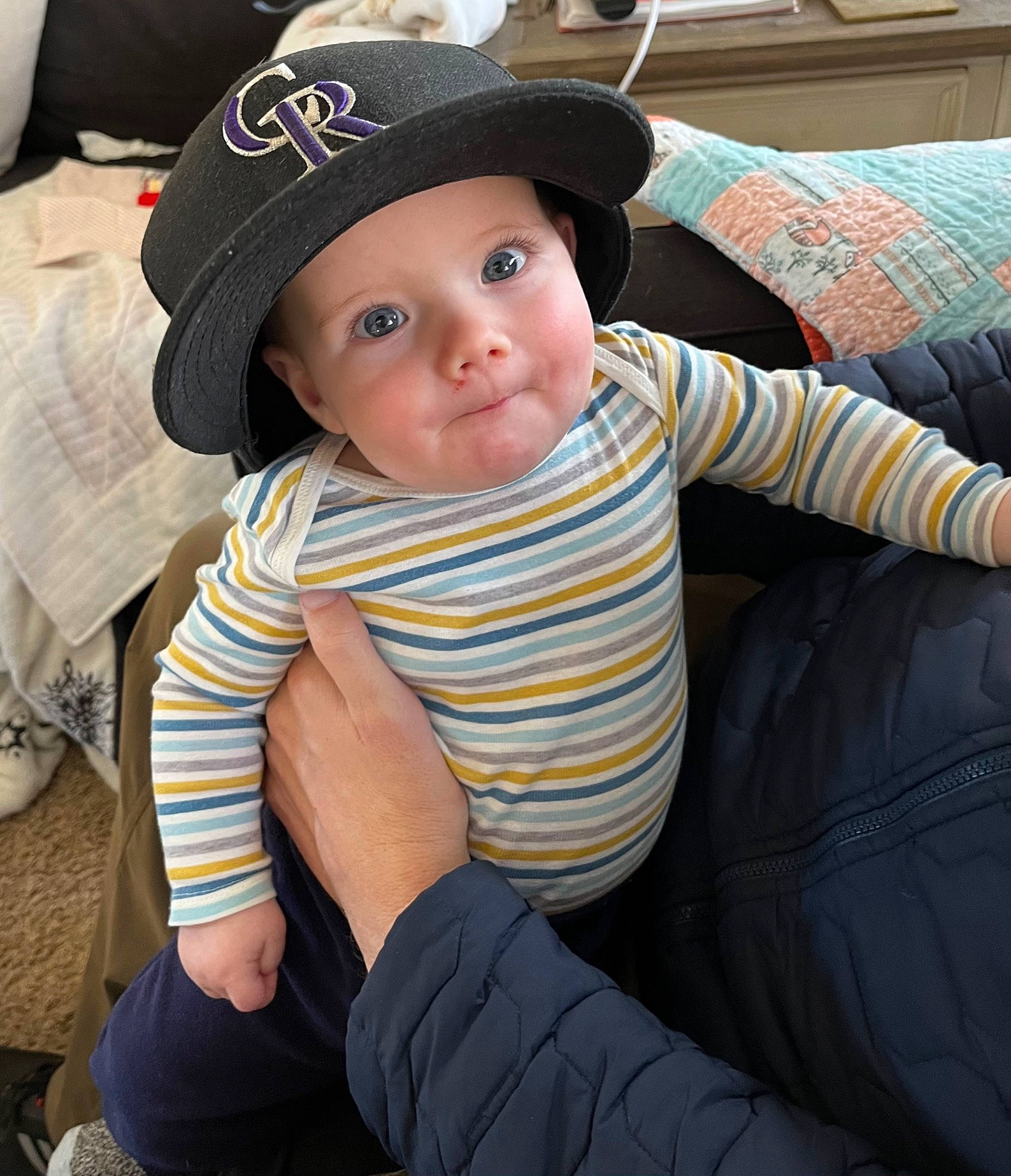 Owen is registered to the contest to win money with this photo: baby, baby_toddler_clothing, baseball_cap, cap, cheek, child, clothing, comfort, elbow, fashion_accessory, hat, headgear, headwear, human_leg, pattern, person, plaid, sitting, sleeve, sun_hat