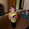 Kaycee is registered to the contest to win money with this photo: child, girl, unicorn, yellow_tank_top, smartphone, barefoot, carpet, laundry_basket, clothes, indoor, door, furniture, cabinet, wall, light_switch, expression, standing, room, technology, casual_clothing
