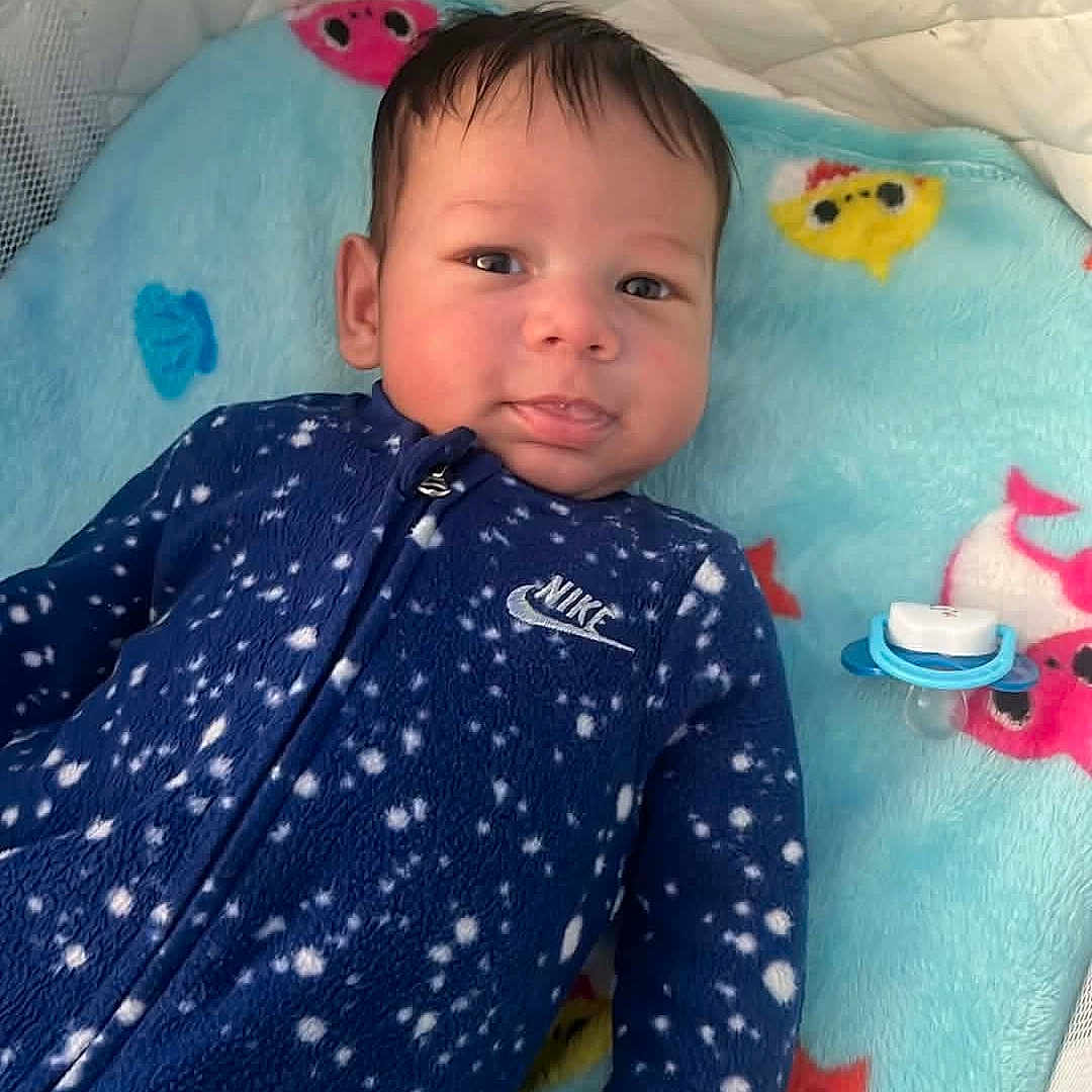 Malakai is registered to the contest to win money with this photo: baby, infant, onesie, blue_clothing, nike, blanket, starfish_pattern, pacifier, crib, cute, lying_down, indoor, face, child, sleepwear, soft_toys, colorful, comfort, baby_bed, portrait