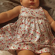 Aurora is registered to the contest to win money with this photo: baby, infant, child, dress, bow, floral_pattern, cute, lying_down, indoors, soft_surface, person, headband, chubby_arms, chubby_legs, skin, face, eyes, legs, arm, clothing
