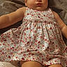 baby, infant, child, dress, bow, floral_pattern, cute, lying_down, indoors, soft_surface, person, headband, chubby_arms, chubby_legs, skin, face, eyes, legs, arm, clothing