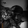 cat, person, portrait, black_and_white, indoor, fluffy, long_hair, pet, human, close_up, selfie, whiskers, eyes, nose, headwear, chain, dramatic_lighting, date_stamp, home, cuddling
