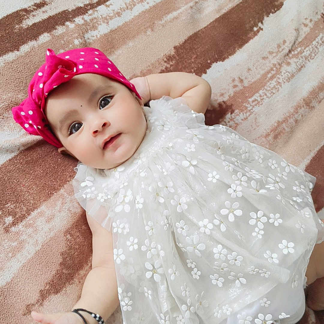 Ajooni is registered to the contest to win money with this photo: adorable, arm, baby, blanket, child, cute, dress, floral, hand, headband, indoors, infant, legs, lying_down, pattern, pink, portrait, skin, soft_texture, white