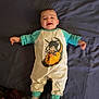 baby, baby_clothes, bed, blanket, cartoon_character, child, clothing, cute, face, happy, indoors, infant, lying_down, onesie, person, portrait, sleepwear, smiling, socks, young_child
