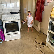 Nélia a rejoint le concours — aidez-le/la à gagner de superbes lots ! child, kid, sunglasses, white_romper, barefoot, kitchen, stove, frying_pan, robe, door, floor, booklet, wall, shelf, container, power_cord, pet_food, bowl, person, indoor