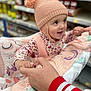 Anaiah is registered to the contest to win money with this photo: aisle, baby, blanket, child, colorful, cute, floral_clothing, happy, holding_hands, indoor, infant, interaction, knit_hat, parent, person, pom_poms, shopping_cart, smiling, store, warm_clothing