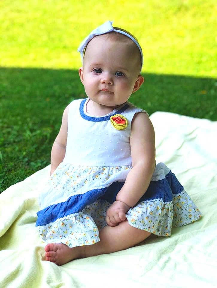Raelynn is registered to the contest to win money with this photo: baby, baby_toddler_clothing, child, dress, grass, hair_accessory, pattern, person, sitting, summer, toddler
