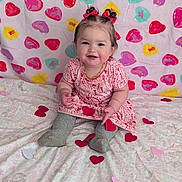 Melody is registered to the contest to win money with this photo: baby, child, girl, smiling, heart, dress, socks, hair_buns, bows, sitting, indoor, playful, cute, happy, decoration, fabric_background, pattern, celebration, portrait, infant