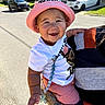 baby, child, smiling, portrait, outdoor, sunny, pink_hat, white_shirt, pink_pants, adult, holding, driveway, residential, cars, houses, beads, toy, happy, close_up, photograph