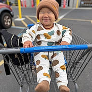 Sincere is registered to the contest to win money with this photo: baby, baby_clothing, beanie, car, child, face, feet, hands, happy, outdoor, pajamas, parking_lot, portrait, pumpkin_pattern, shopping, shopping_cart, sitting, smiling, store_entrance, supermarket