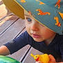toddler, child, blue_eyes, hat, sun_hat, animal_print, rubber_duck, inflatable_pool_toy, green, wooden_deck, outdoor, summer, play, toy, cute, close_up, person, baby, sunlight, curious