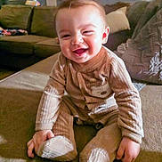 River is registered to the contest to win money with this photo: baby, child, smiling, indoors, pajamas, couch, living_room, cute, happy, infant, seated, cozy, face, hands, footed_pajamas, home, childhood, portrait, young, comfortable