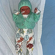 Teddie is registered to the contest to win money with this photo: newborn, baby, infant, knitted_hat, knitted_cardigan, animal_print, hospital, medical_tube, lying_down, white_sheet, cute, small, clothing, child, face, person, footed_pajamas, indoors, resting, baby_mittens