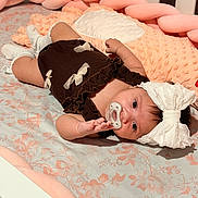 Zoe is registered to the contest to win money with this photo: baby, infant, child, lying_down, pacifier, bow, headband, dress, white_socks, nursery, crib, bed, bedding, floral_pattern, pink, portrait, indoors, cozy, happy, face