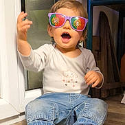 Solan a rejoint le concours — aidez-le/la à gagner de superbes lots ! toddler, child, sunglasses, indoor, barefoot, jeans, long_sleeve_shirt, floor, gesture, happy, person, casual_clothing, reflection, flag, purple_sunglasses, home, smile, cute, seated, footwear
