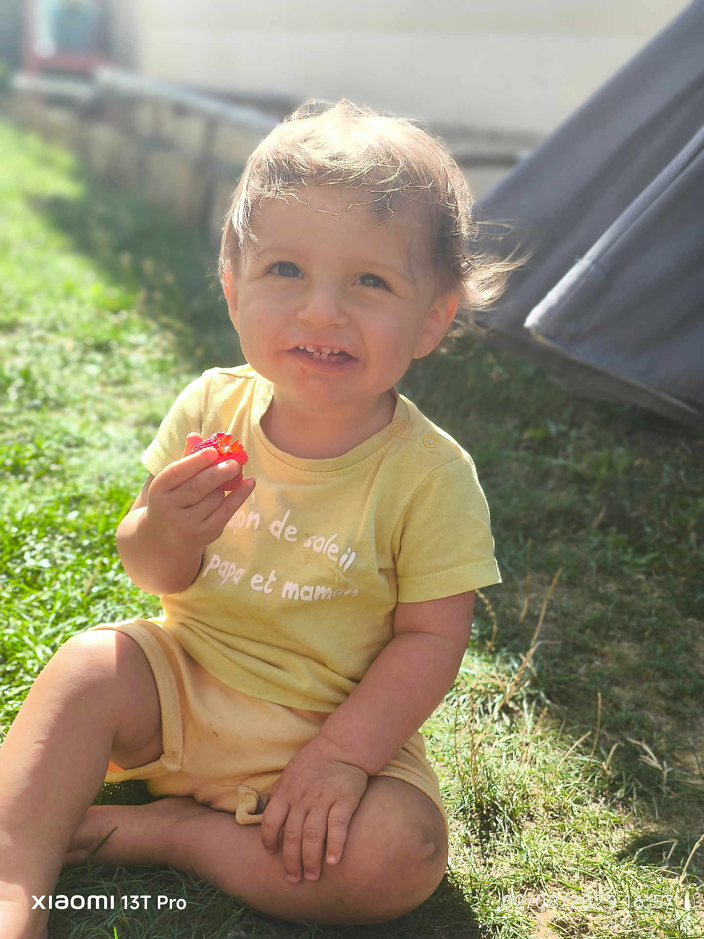 Solan participe au concours pour gagner de l'argent avec cette photo : child, toddler, smiling, grass, outdoor, sunlight, yellow_clothing, berry, happy, sitting, nature, baby, casual, cute, portrait, daylight, face, hands, grass_field, playful