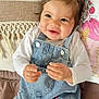 baby, child, smiling, denim_overalls, pigtails, red_hair_ties, couch, pillow, cozy, indoor, cute, happy, portrait, toddler, clothing, hands, face, hair, seated, comfortable