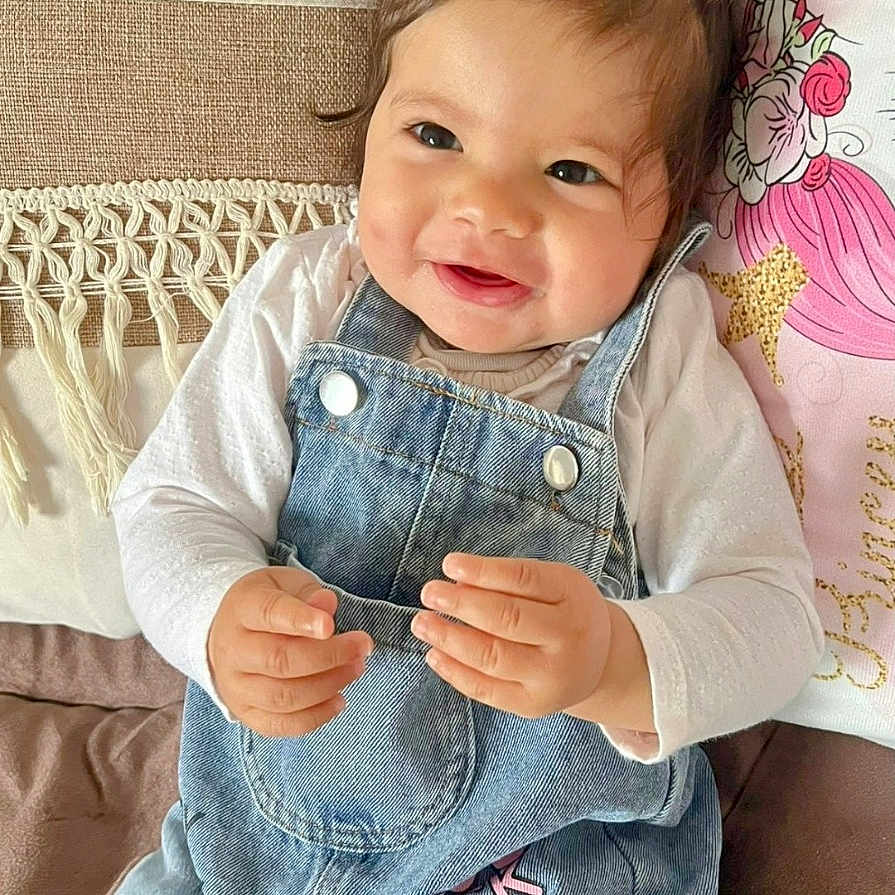 Ghazal participe au concours pour gagner de l'argent avec cette photo : baby, child, clothing, comfortable, couch, cozy, cute, denim_overalls, face, hair, hands, happy, indoor, pigtails, pillow, portrait, red_hair_ties, seated, smiling, toddler