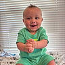 baby, blanket, child, clapping, cute, expression, face, green_clothing, hands, happy, indoor, infant, light, natural_light, patterned_blanket, portrait, sitting, smiling, toddler, window_blinds