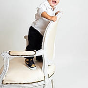 Liam is registered to the contest to win money with this photo: toddler, child, smiling, standing, white_chair, white_background, black_pants, white_shirt, sneakers, nike, happy, portrait, studio_photo, furniture, young_child, indoors, person, cute, fashion, playful