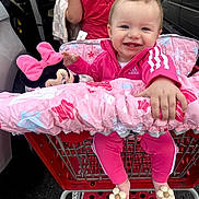 Ellie joined the competition — help win amazing prizes! baby, child, shopping_cart, pink_clothing, plush_toy, minnie_mouse, smiling, happy, person, parking_lot, car, blanket, footwear, baby_shoes, outdoor, toy, clothing, basket, head, face