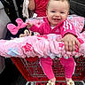 baby, child, shopping_cart, pink_clothing, plush_toy, minnie_mouse, smiling, happy, person, parking_lot, car, blanket, footwear, baby_shoes, outdoor, toy, clothing, basket, head, face