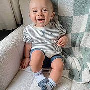 Asher joined the competition — help win amazing prizes! baby, smiling, child, sitting, chair, blanket, striped_shirt, socks, happy, indoor, cute, portrait, cozy, furniture, infant, leg, hand, face, blue_shorts, home