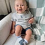 baby, smiling, child, sitting, chair, blanket, striped_shirt, socks, happy, indoor, cute, portrait, cozy, furniture, infant, leg, hand, face, blue_shorts, home