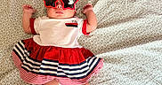 Lillie is registered to the contest to win money with this photo: accessories, baby, blue, celebration, child, cute, dress, fashion, flower, headband, indoors, infant, lying_down, patterned_blanket, person, portrait, red, socks, sunglasses, white