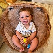 Matheo participe au concours pour gagner de l'argent avec cette photo : baby, child, smiling, toy, cushion, furry, lion, indoor, floor, wooden_floor, happy, cute, sitting, white_shirt, playful, infant, room, furniture, colorful, holding