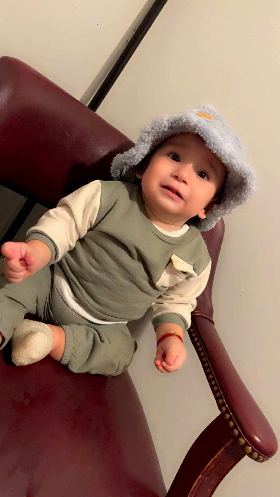Yelimar joined the competition — help win amazing prizes! toddler, child, hat, bucket_hat, sitting, chair, leather_chair, clothing, long_sleeve, pants, footwear, sock, indoor, person, cute, expression, face, hand, curious, cozy