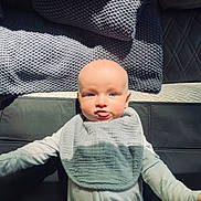 Hudson is registered to the contest to win money with this photo: baby, infant, tongue_out, pajamas, bib, blanket, soft_light, indoor, child, cute, playful, face, head, person, skin, expression, lying_down, cozy, texture, closeup
