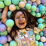 child, smiling, laughing, ball_pit, balls, pastel_colors, tshirt, long_hair, playful, happy, indoors, fun, cute, colorful, portrait, person, casual_clothing, joyful, face, recreation