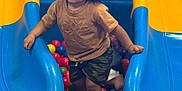 Jahmarii joined the competition — help win amazing prizes! child, toddler, curly_hair, ball_pit, slide, blue, yellow, colorful, playground, indoor, fun, play, smiling, clothing, shorts, tshirt, person, hands, legs, happy