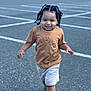 toddler, child, running, smiling, braided_hair, brown_tshirt, shorts, green_shoes, parking_lot, outdoor, asphalt, daylight, happy, person, casual_clothing, playful, young_child, cute, motion, fun