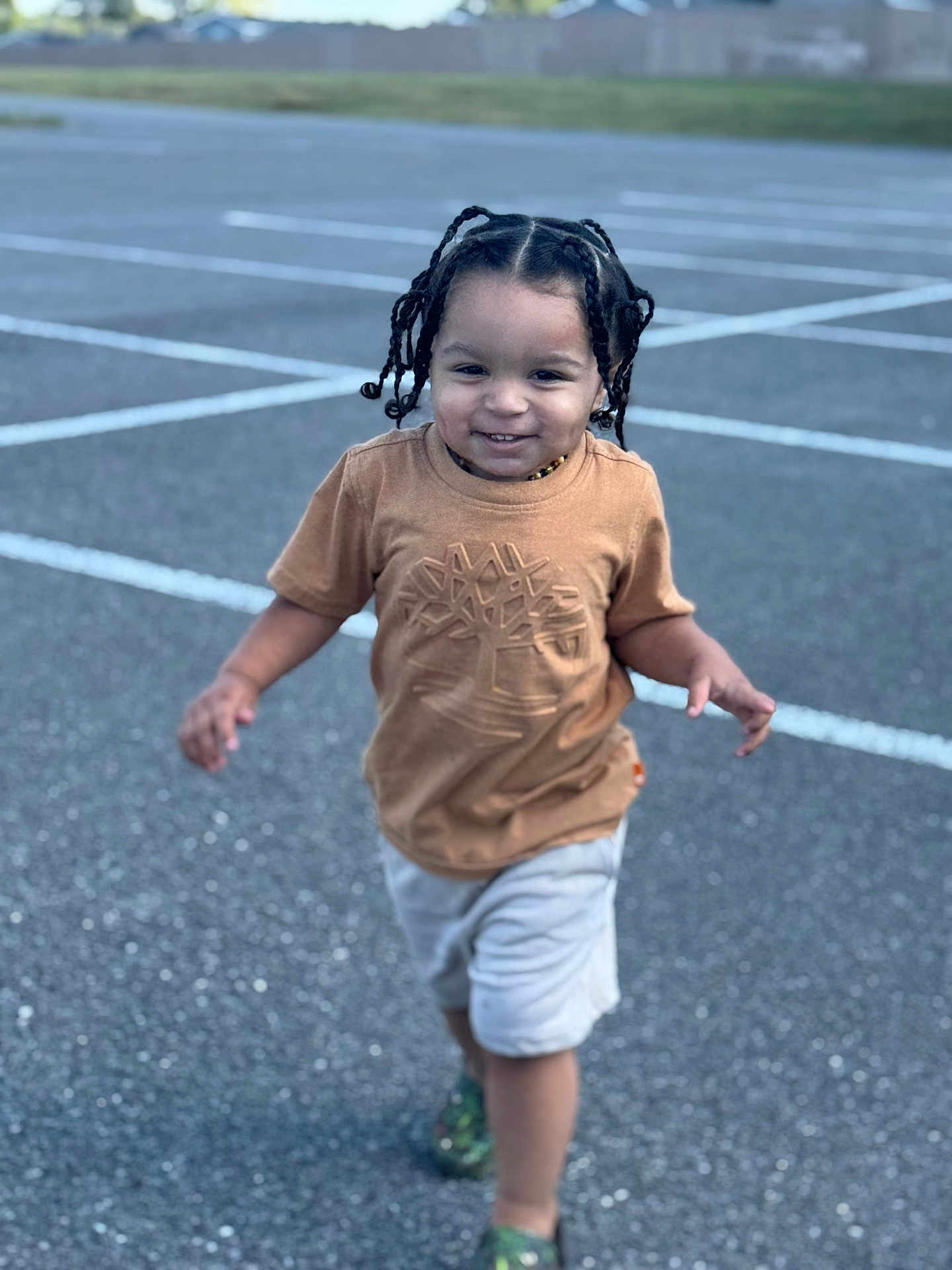 Jahmarii is registered to the contest to win money with this photo: toddler, child, running, smiling, braided_hair, brown_tshirt, shorts, green_shoes, parking_lot, outdoor, asphalt, daylight, happy, person, casual_clothing, playful, young_child, cute, motion, fun