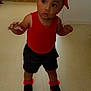 toddler, child, indoor, red_clothing, hair_bows, curly_hair, black_shoes, floor, kitchen, cabinet, microwave, curious, standing, shorts, young_child, person, baby, home, walking, expression