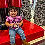 toddler, child, smiling, purple_shirt, minnie_mouse, jeans, boots, christmas_trees, holiday_decor, red_platform, indoor, shopping_mall, festive, happy, cute, young_child, casual_clothing, winter_boots, decorations, portrait