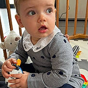 Inès a rejoint le concours — aidez-le/la à gagner de superbes lots ! toddler, child, toy, playpen, cushion, plush_toy, indoor, curious, blond_hair, collared_shirt, polka_dots, sitting, floor_mat, long_sleeve, blue_tights, expression, looking_away, hands, baby, play