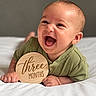 baby, infant, child, smiling, laughing, portrait, bed, bedding, white_sheets, green_clothing, wooden_sign, milestone, three_months, indoors, close_up, face, hands, happy, sitting, photography