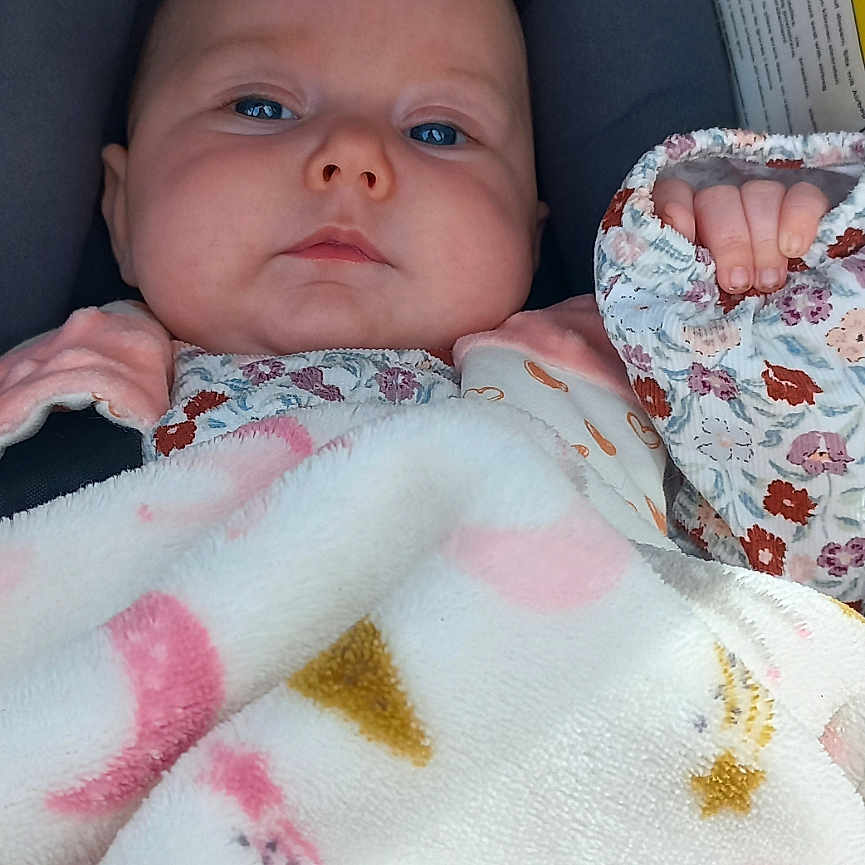 Anaël a rejoint le concours — aidez-le/la à gagner de superbes lots ! baby, blanket, blue_eyes, cushion, face, infant, pink, pattern, resting, seat, serious, soft_texture, warning_label, young_child, floral_sleeve, cozy, indoor, portrait, closeup, child