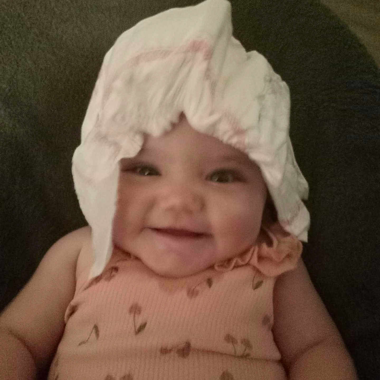 Everly is registered to the contest to win money with this photo: baby, child, smiling, diaper, headwear, peach_outfit, floral_print, cute, infant, portrait, happy, sitting, indoors, soft_lighting, clothing, face, chubby_cheeks, funny, playful, person