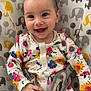 baby, smiling, infant, floral_clothing, onesie, baby_seat, elephant_pattern, happy, child, cute, face, hands, sitting, indoor, colorful, patterned_fabric, young, portrait, baby_girl, joyful