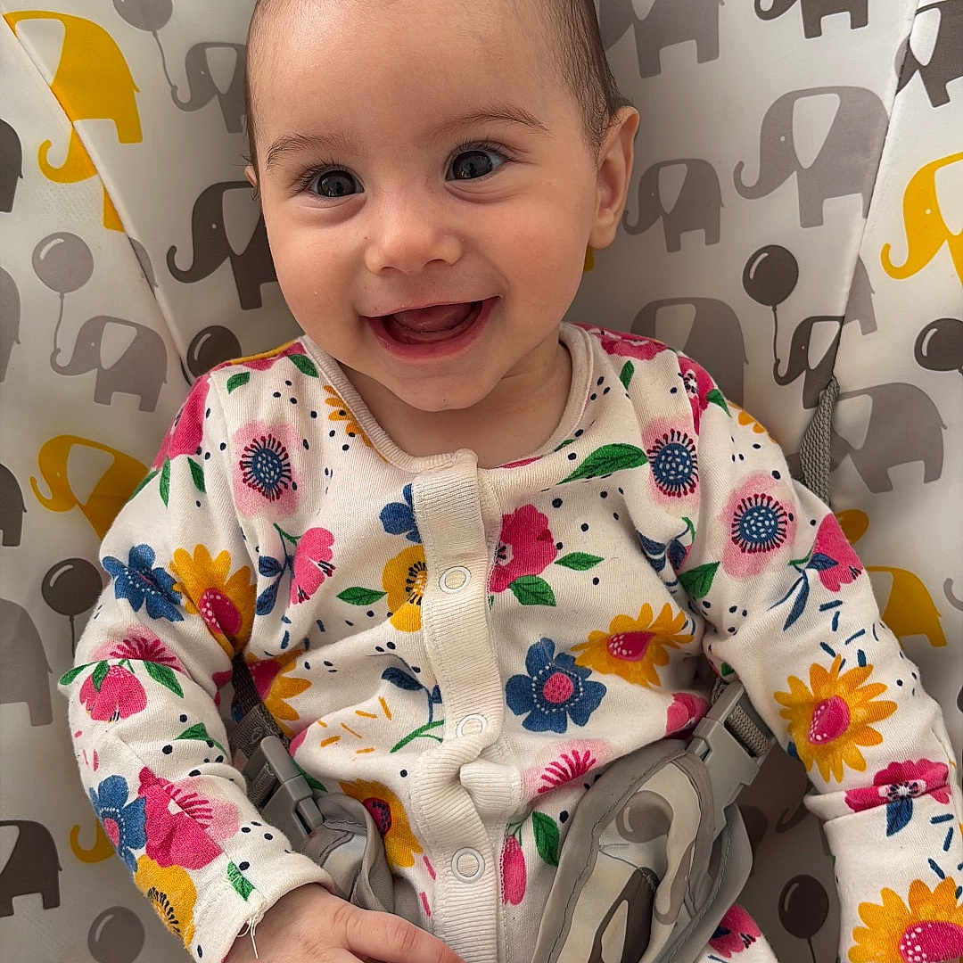 Hîvda Róisín joined the competition — help win amazing prizes! baby, baby_girl, baby_seat, child, colorful, cute, elephant_pattern, face, floral_clothing, hands, happy, indoor, infant, joyful, onesie, patterned_fabric, portrait, sitting, smiling, young