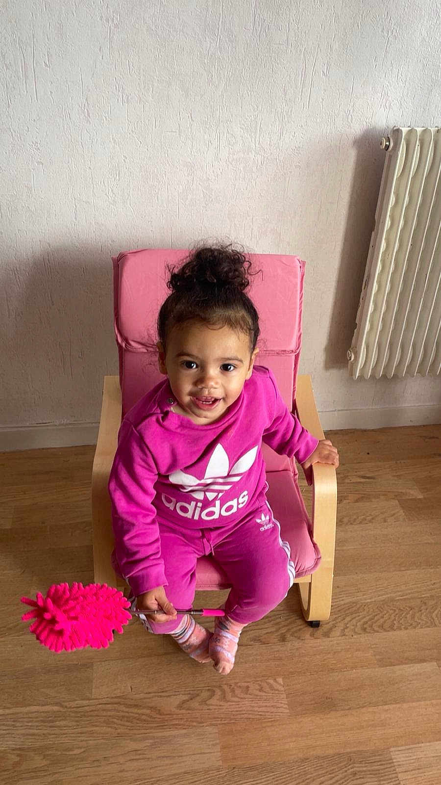 Kamélia participe au concours pour gagner de l'argent avec cette photo : toddler, child, pink_clothing, adidas, chair, indoor, wooden_floor, radiator, duster, smiling, curly_hair, socks, person, furniture, happy, casual, portrait, young_child, seated, playful